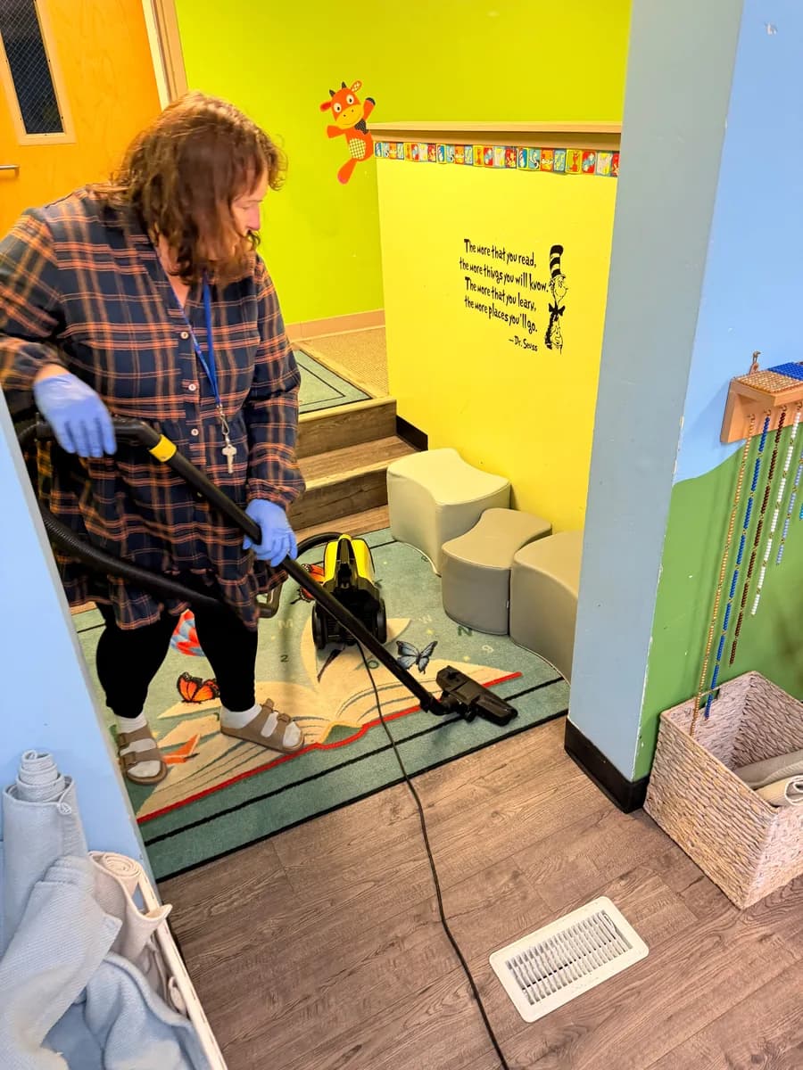 Crew member vacuuming a classroom rug at a Montessori childcare school in Kirkland