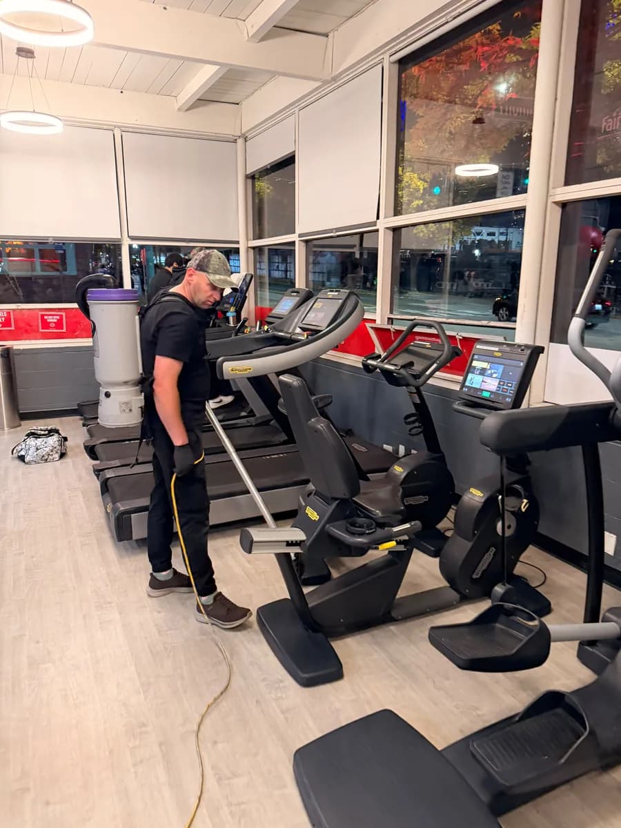 Crew member vacuuming the cardio area of a Seattle gym with a backpack vacuum
