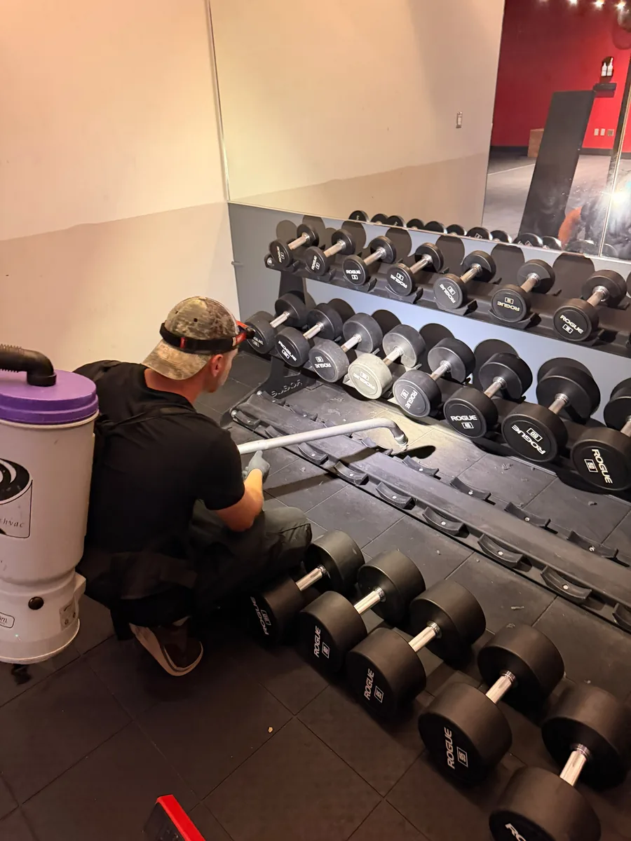 Vacuuming under a dumbbell rack during the Transform 180 gym deep clean