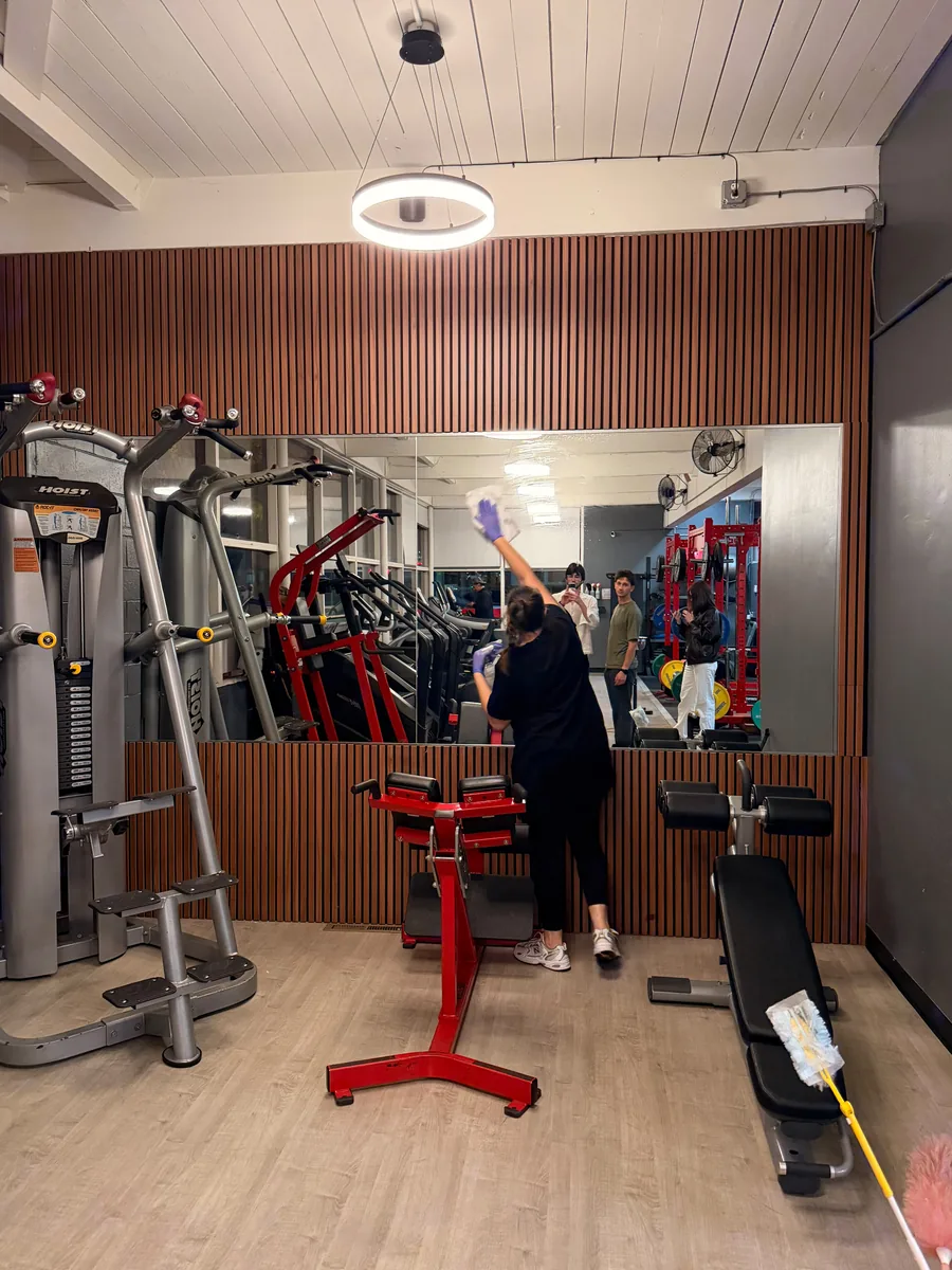 Crew member dusting the top of a mirror wall above strength machines