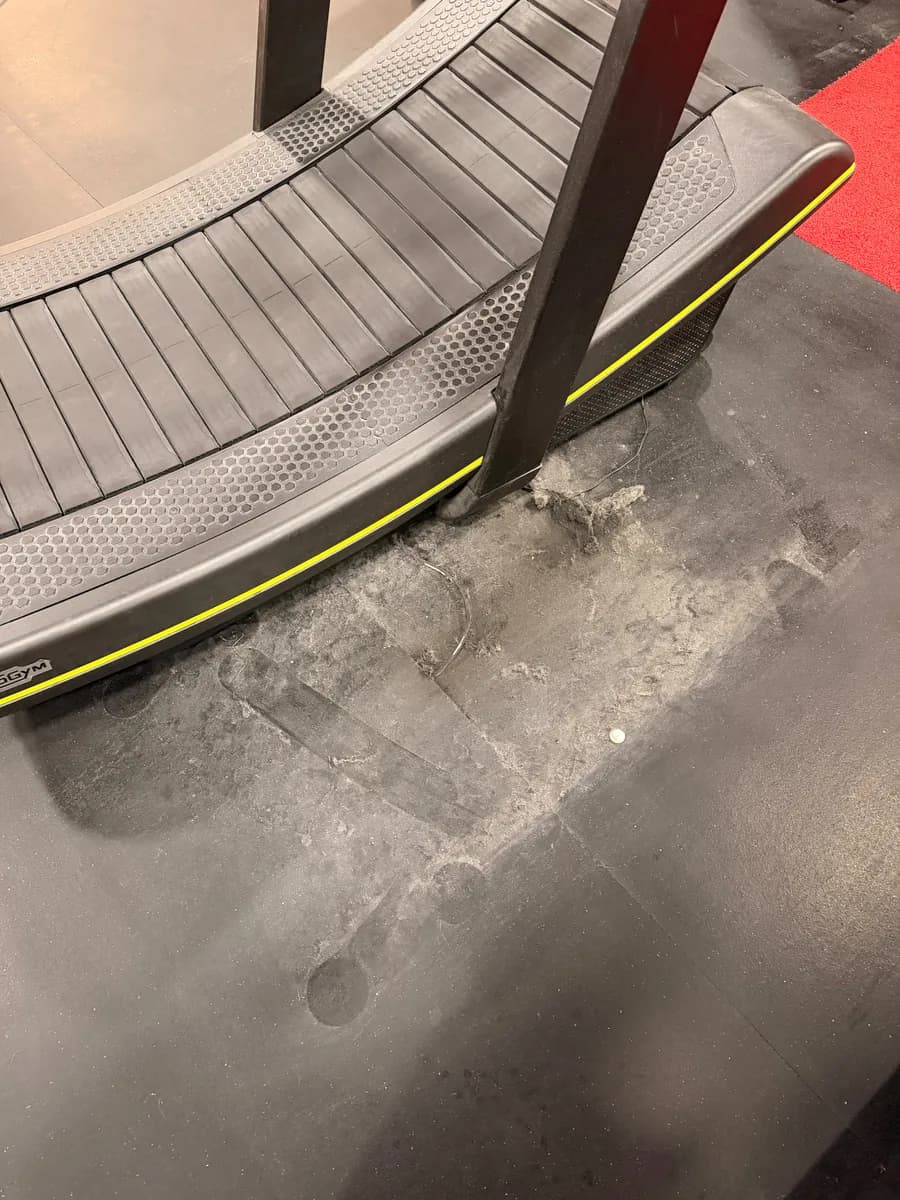 Dust and debris on the gym floor under a curved treadmill after the machine was moved