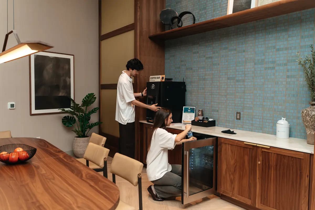 Two crew members cleaning a coffee bar and cabinetry in a common area