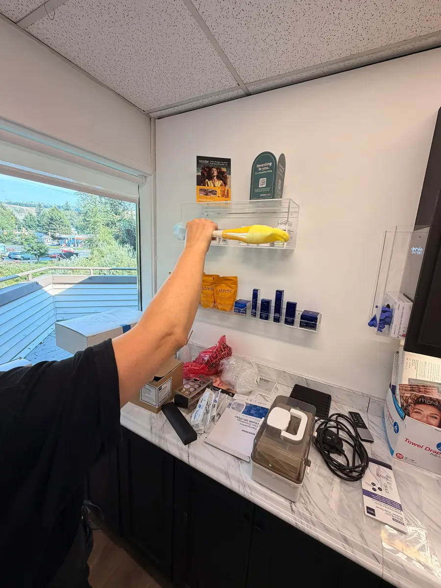 Dusting product shelving at Sherisse Hill Aesthetic Derm during a weekly clean
